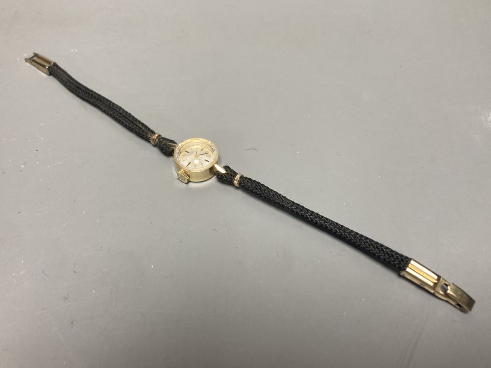 A ladys 14k Omega manual wind wrist watch, on twin strand fabric strap, case diameter 13mm ex. crown, gross 7 grams.
